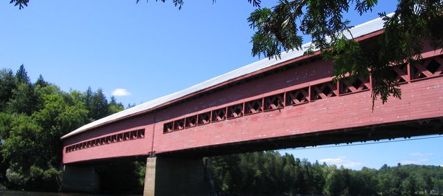 a red covered bridge several people are in mid air jumping off
