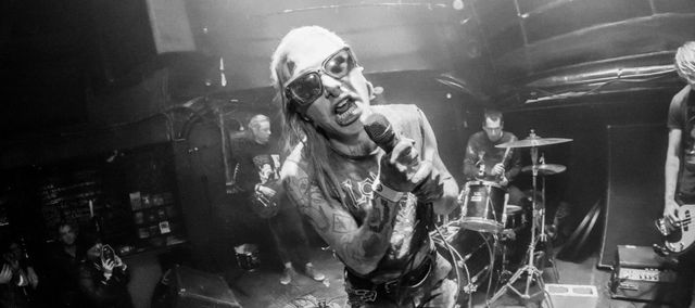 spacers playing on a stage, from a fisheye camera, the singer is wearing sunglasses screaming right in your face