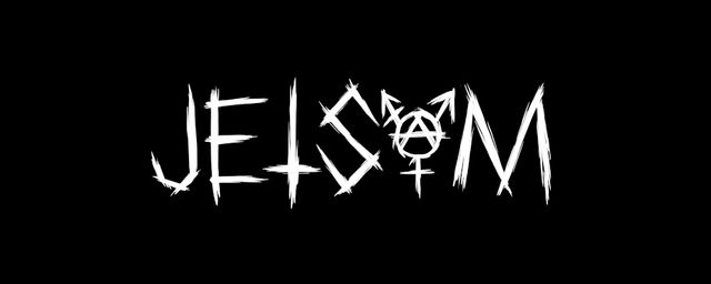 black and white image of Jetsam, 3 of them, sitting on the floor. they all have glasses and dark hair. one lone and straight, one short under a cap, one long and frizzy. they look serious.